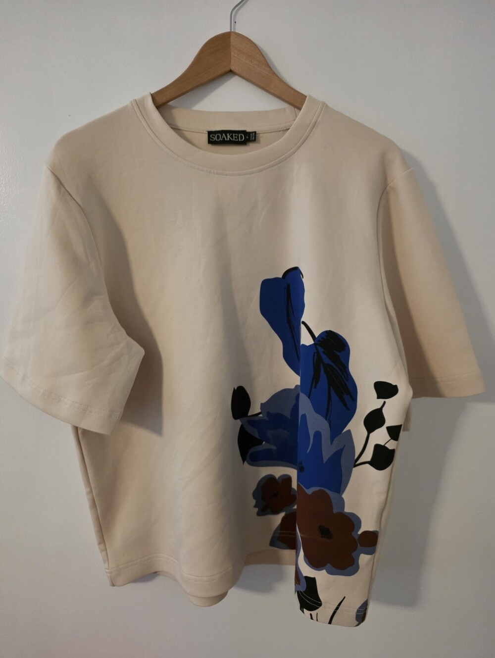 Soaked in Luxury tee features a striking blue floral graphic sandy Beige